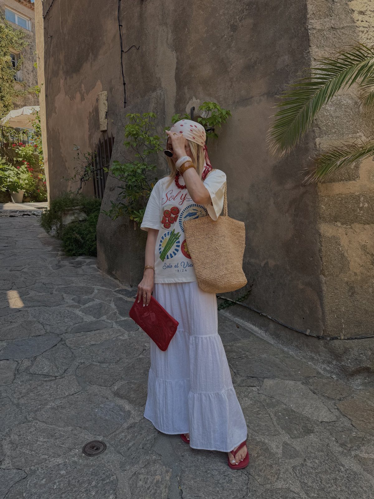 Person in a white graphic tee and long white tiered skirt walking on a cobblestone street.