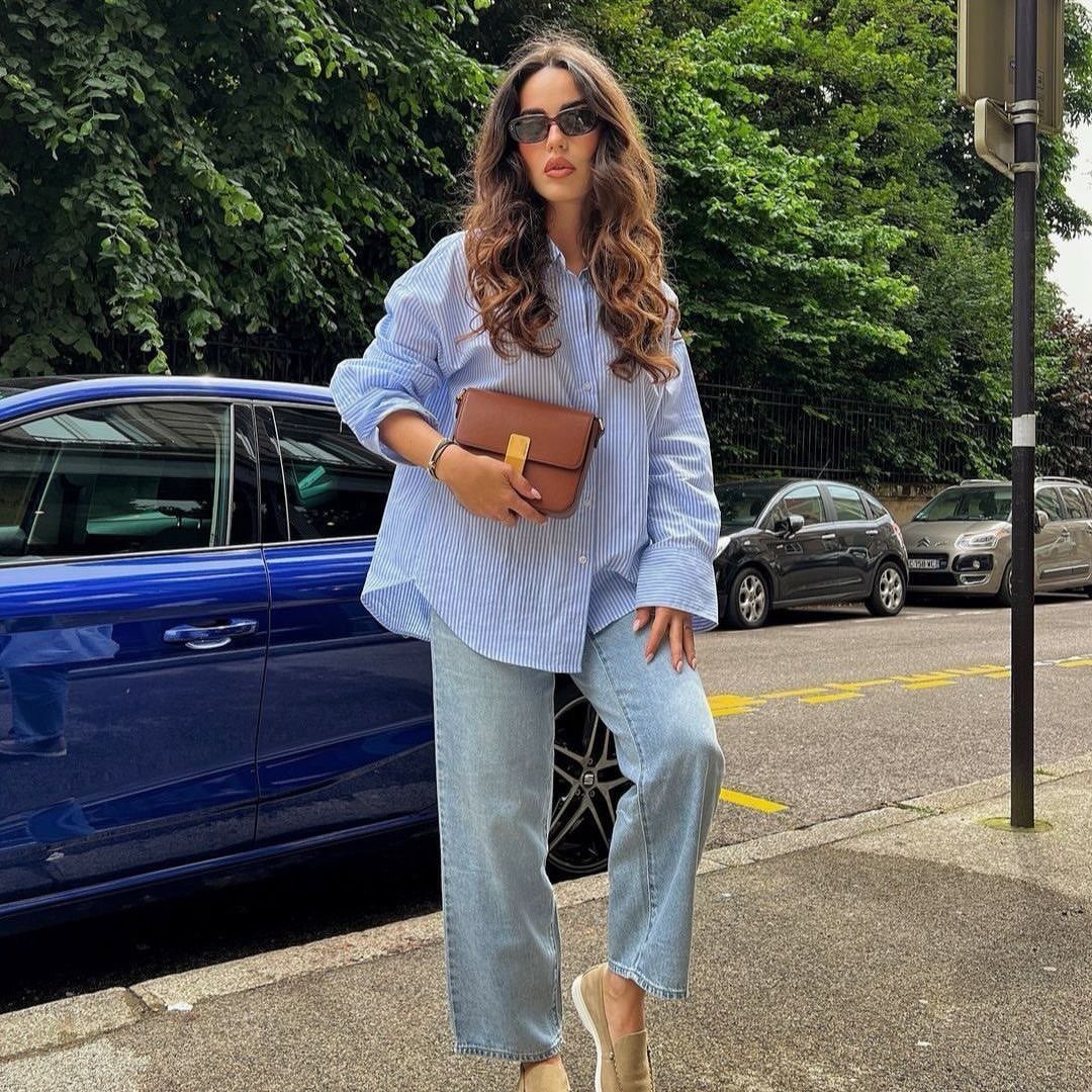 Woman in a striped button-down shirt and wide-leg denim jeans standing on a city street.
