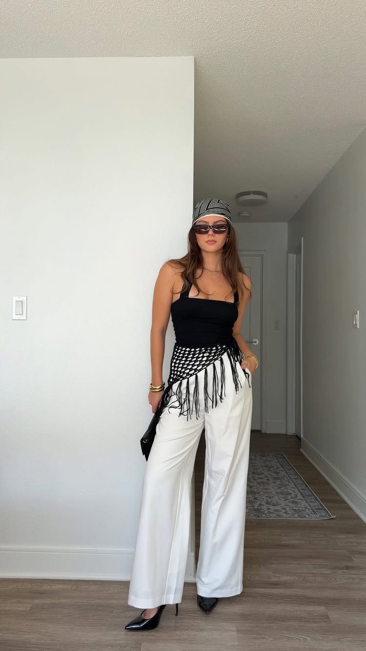 Woman wearing a black tank top and white wide-leg pants with a patterned waist scarf.