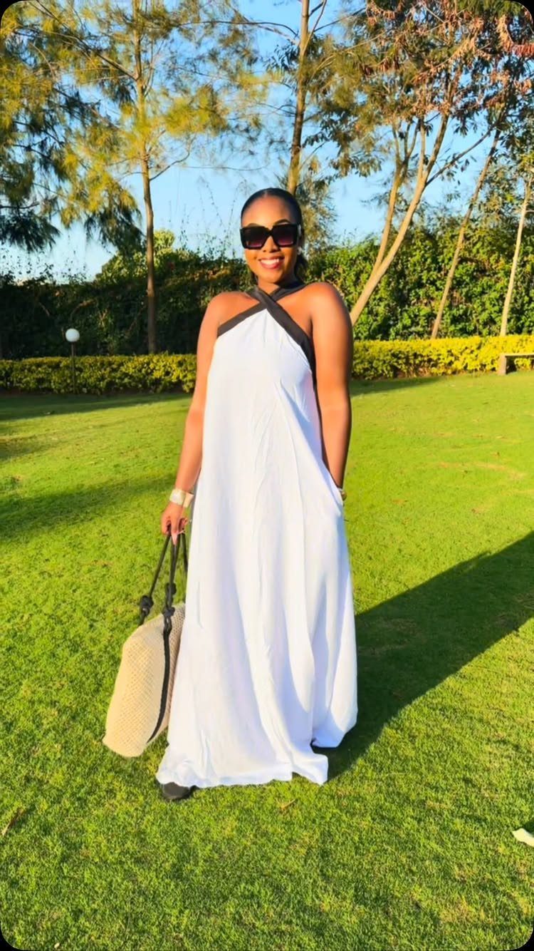 A woman in a long white halter maxi dress standing on a sunny green lawn.