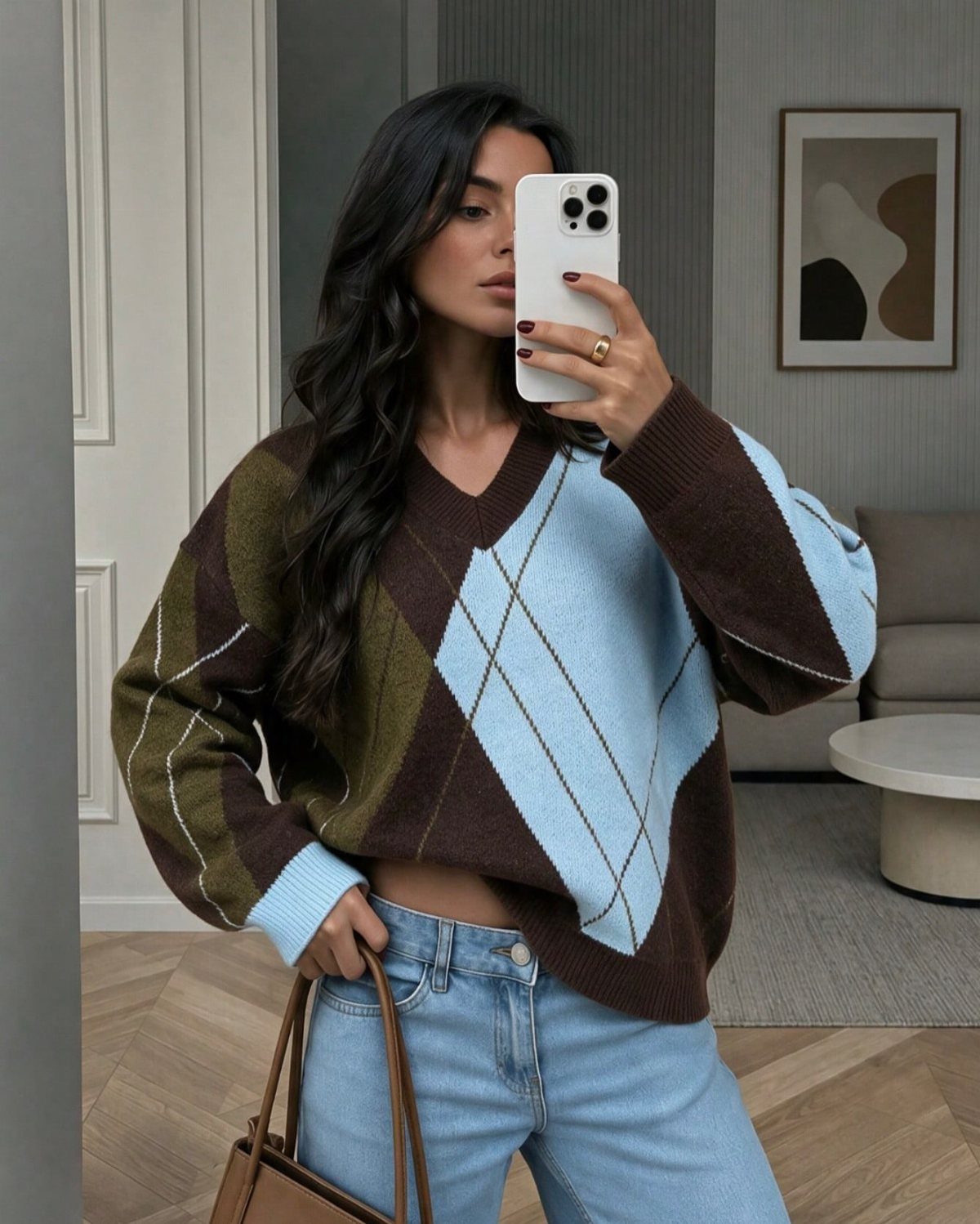 Woman in an argyle pattern V-neck sweater and blue jeans taking a mirror selfie.