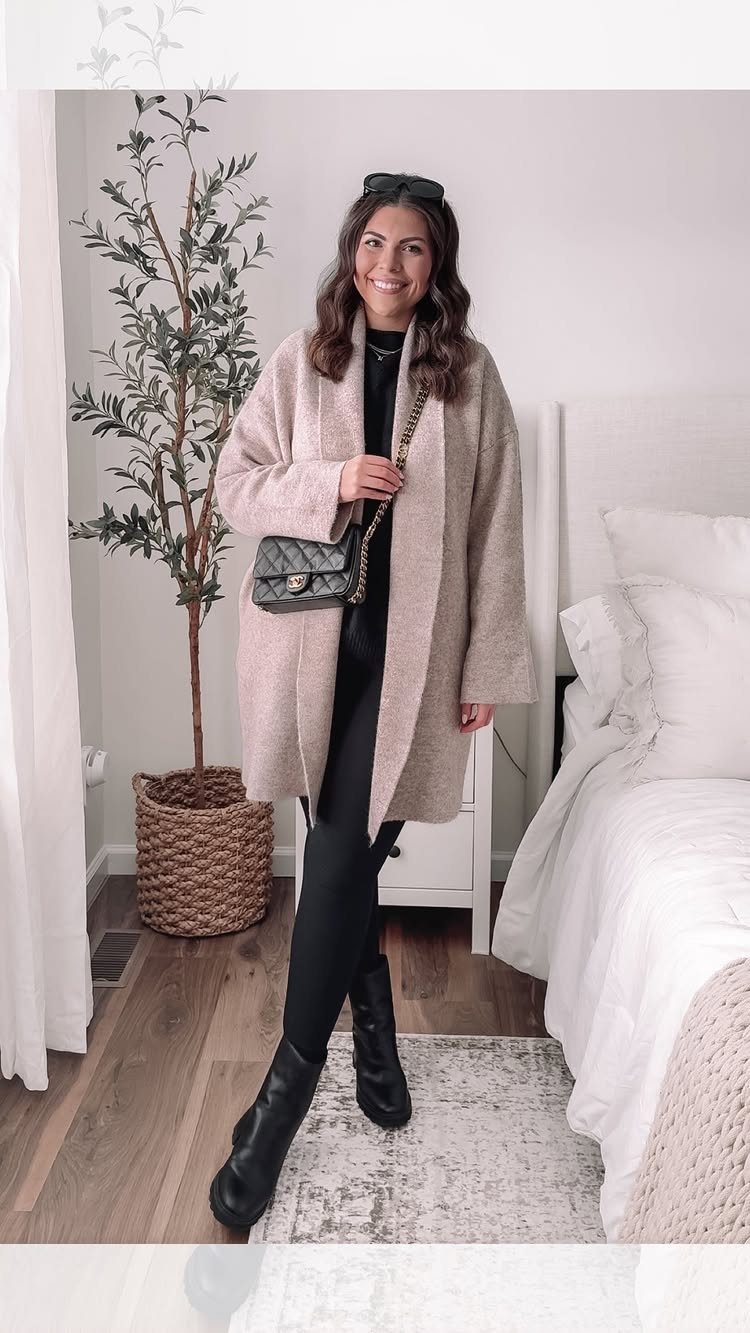 A woman wearing a long beige cardigan, black turtleneck, leggings, and black boots.
