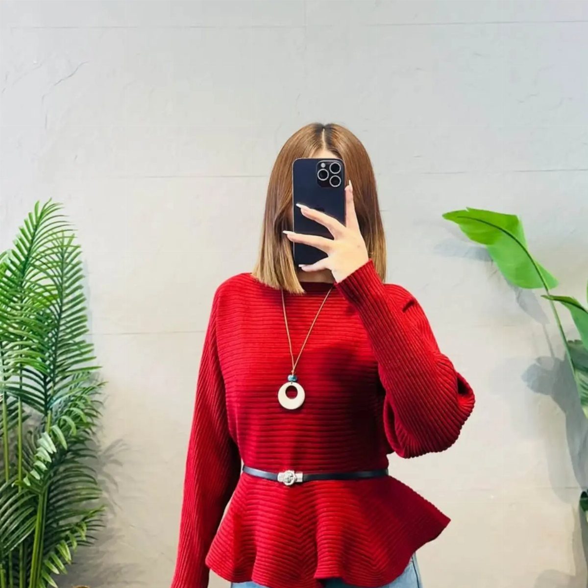 A person wearing a red ribbed peplum sweater and a black belt while taking a selfie.