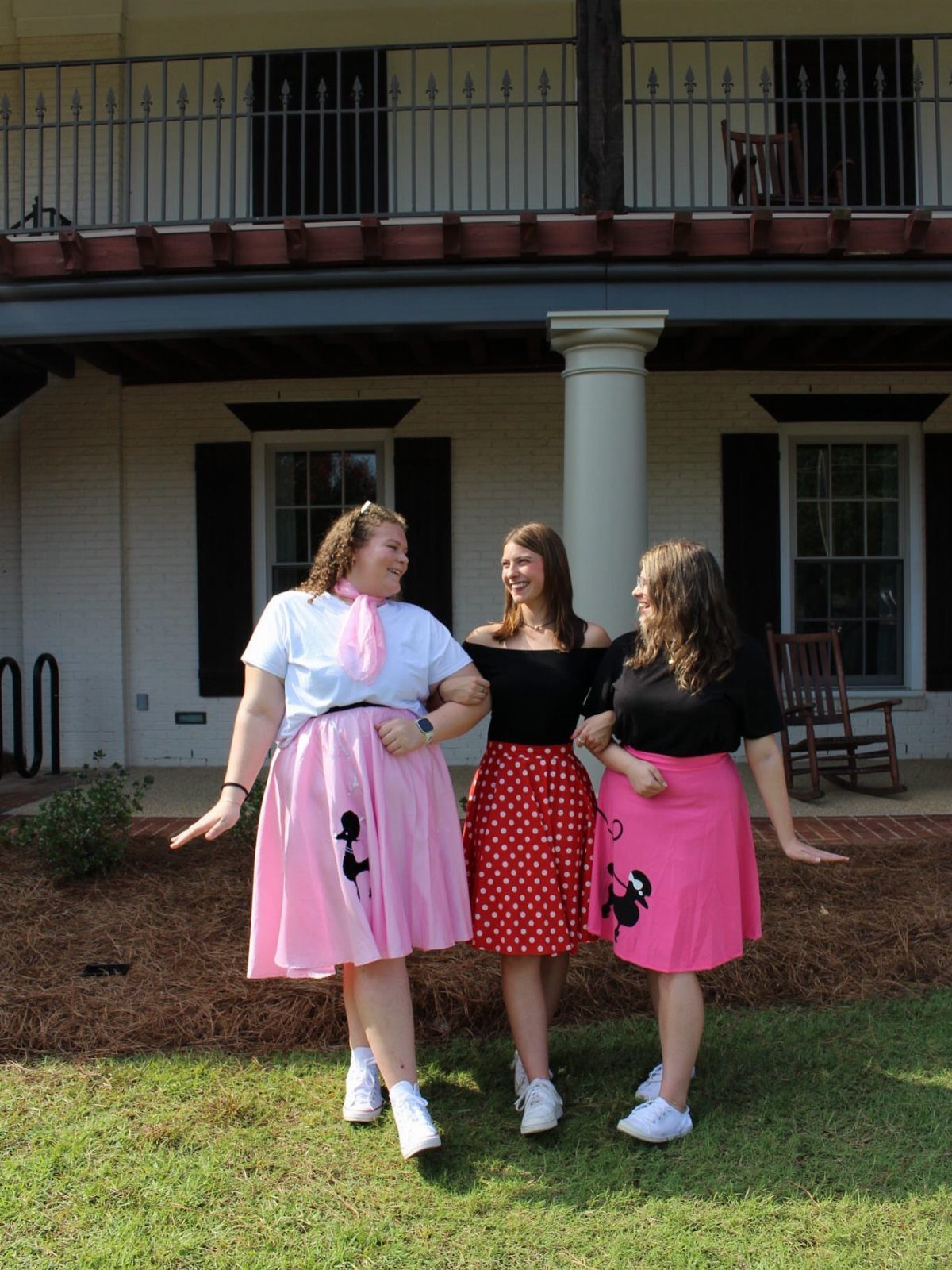 Three women wearing colorful 1950s style flared poodle skirts standing on a green lawn.