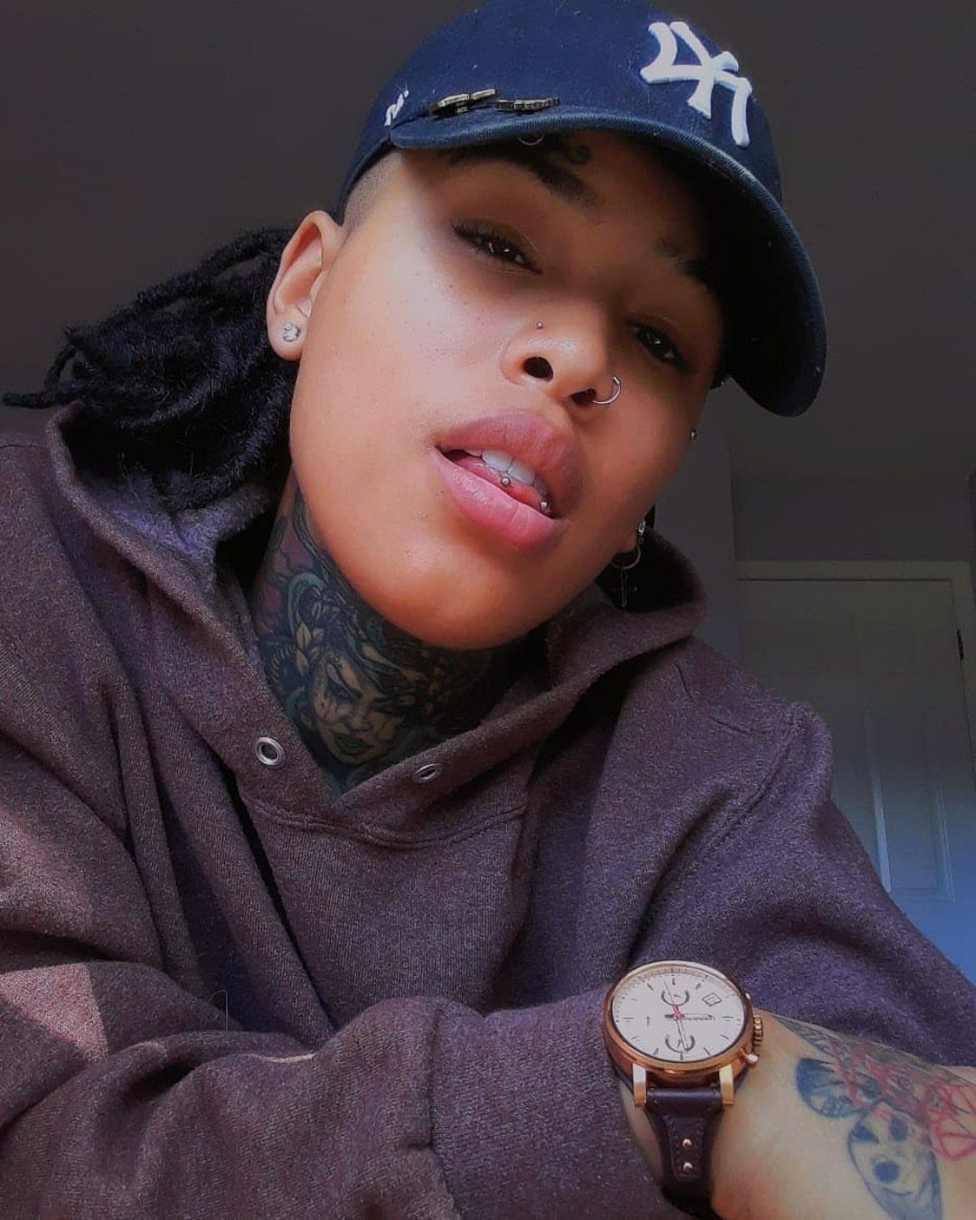 A person wearing a navy blue baseball cap and a brown hoodie looking at the camera.