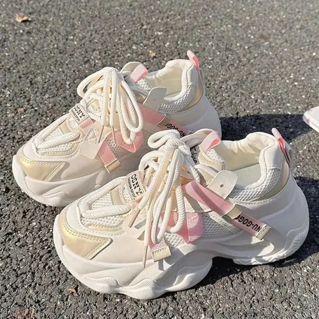 Cream and pink chunky sneakers with thick soles sitting on an asphalt ground.