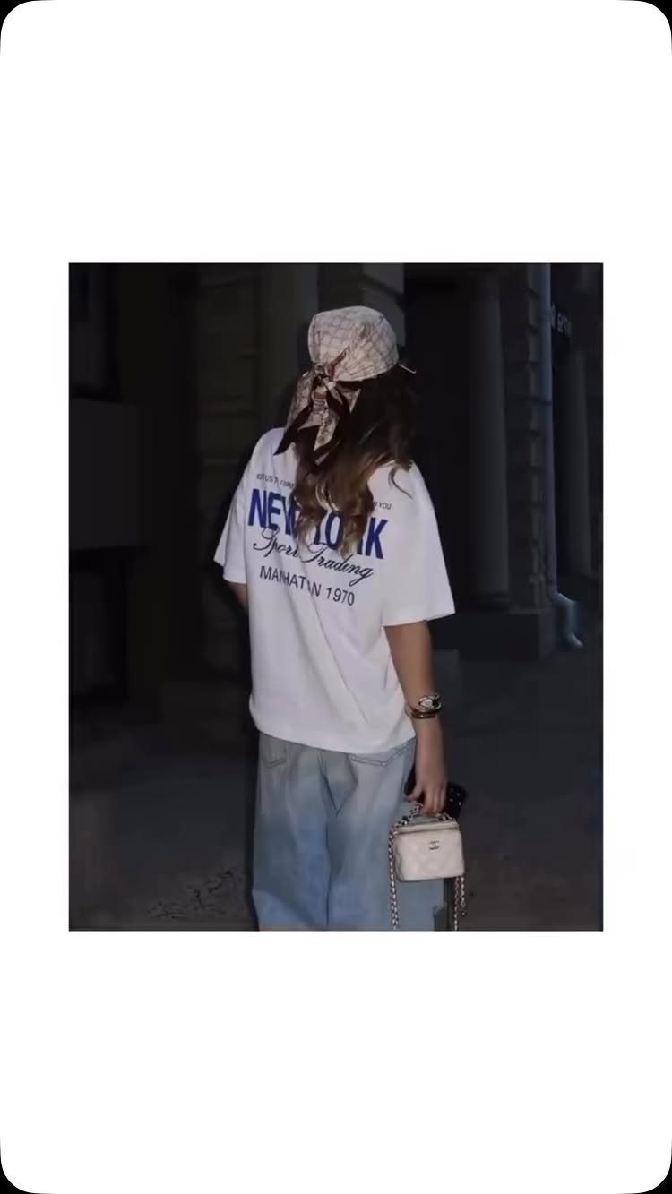 Person wearing an oversized white graphic t-shirt and light blue denim jeans at night.