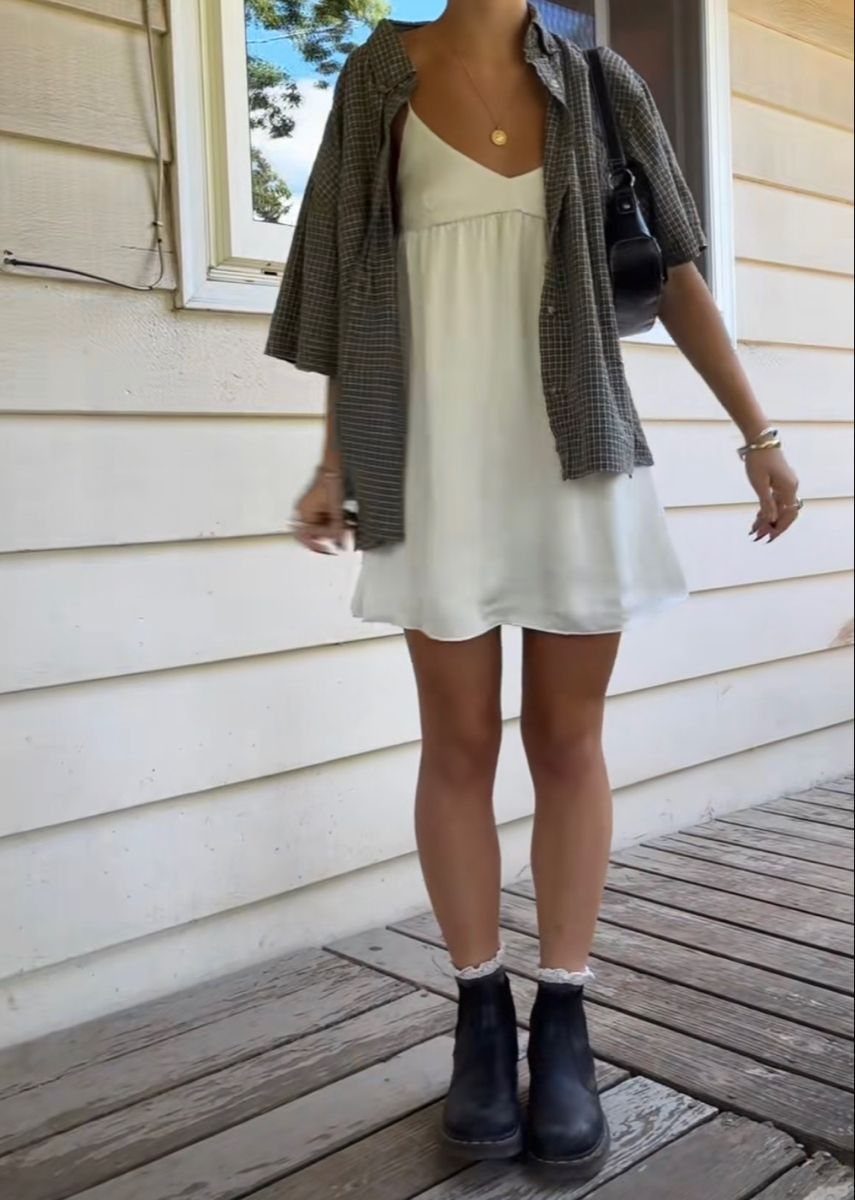 A person wearing a white mini dress, a dark plaid flannel shirt, and black boots.