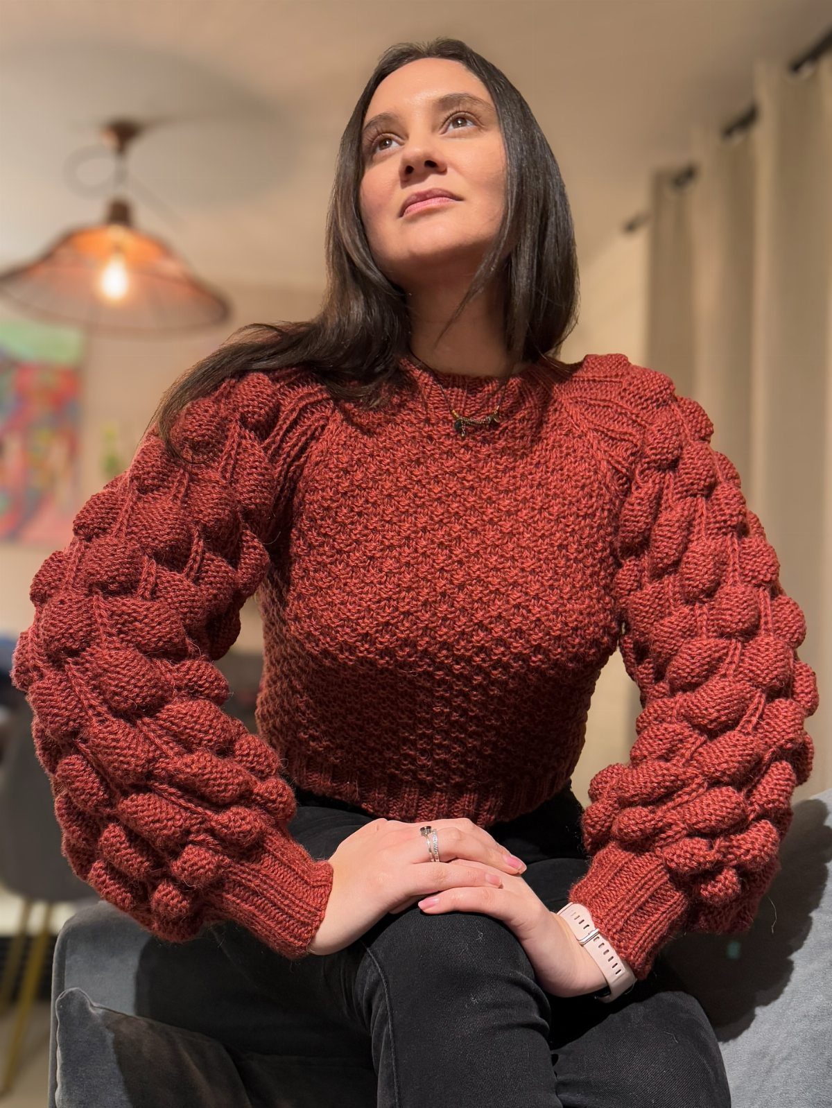 A woman wearing a textured rust-colored bobble knit sweater with large puff sleeves.