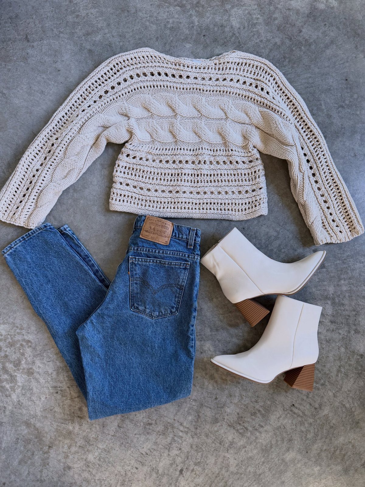 White ankle boots with brown heels paired with a cream sweater and blue jeans.