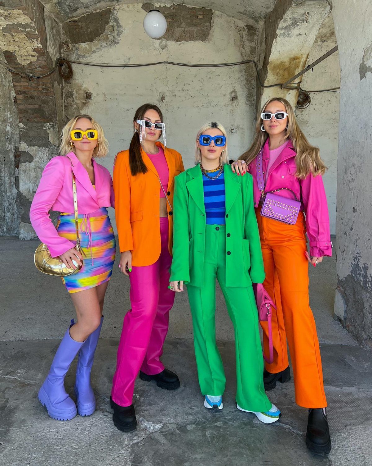 Four women posing in vibrant, brightly colored monochromatic fall outfits against a stone wall.