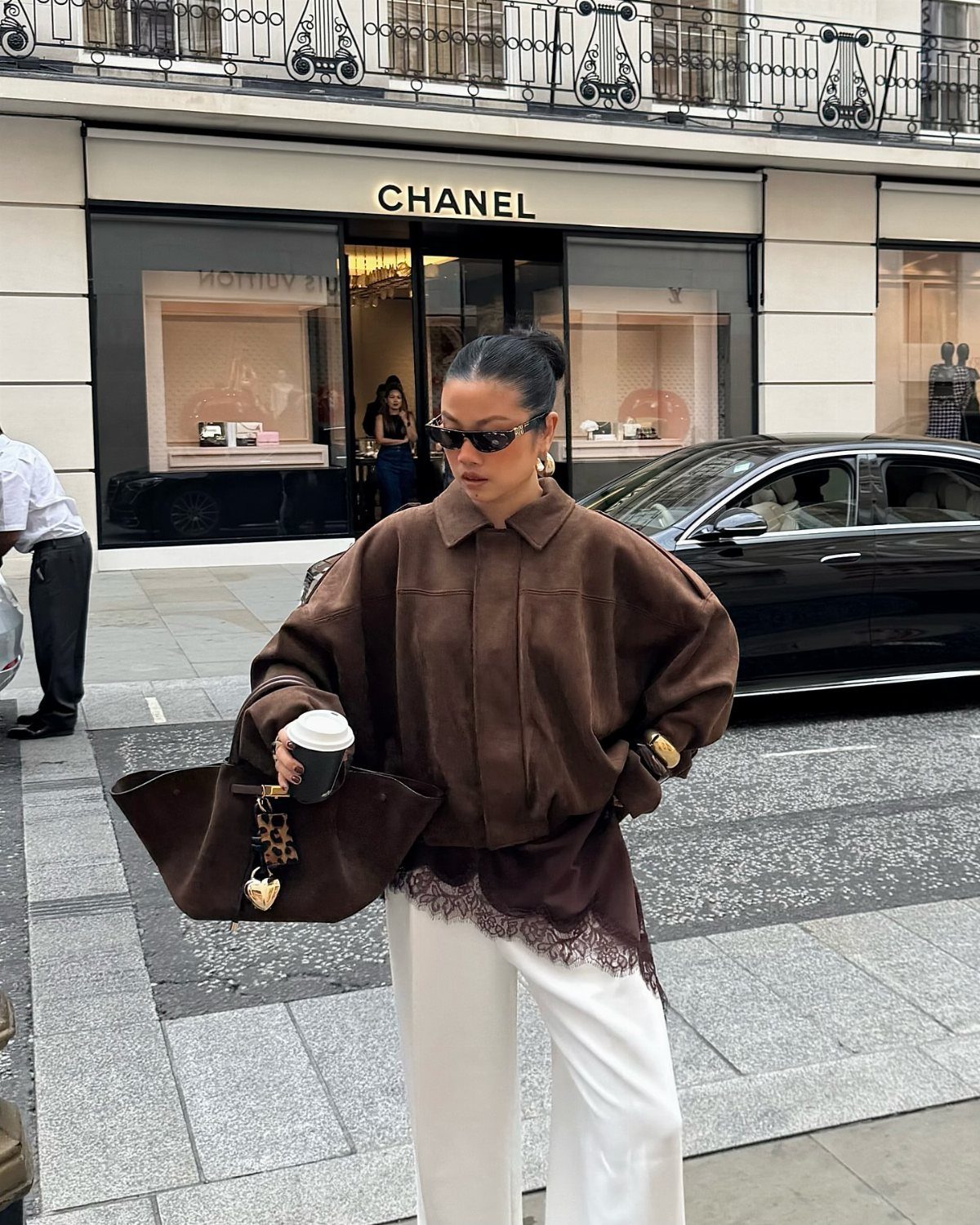 Woman in a brown lace-trimmed shirt and white trousers walking on a city street.