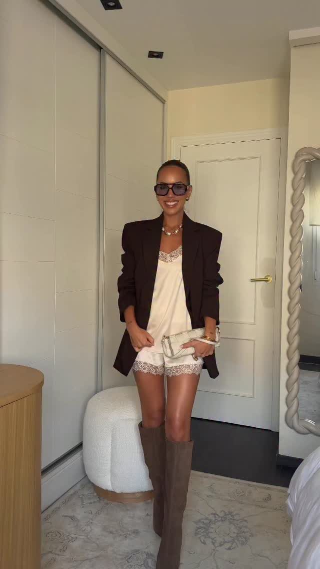 A woman wearing a dark blazer over a white lace outfit and tall brown boots.