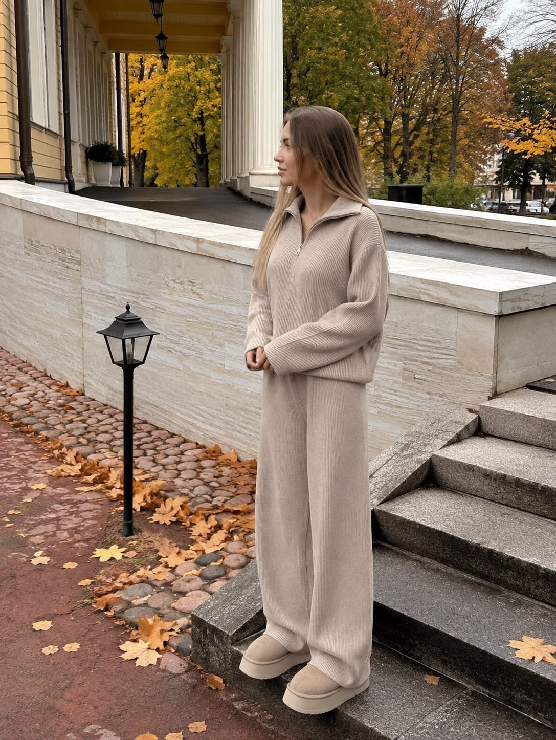 Woman wearing a matching beige ribbed knit sweater and wide-leg trousers standing on stone steps.
