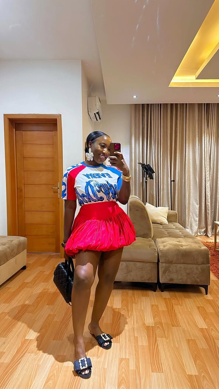 A woman posing in a mirror wearing a graphic t-shirt and a bright pink bubble skirt.