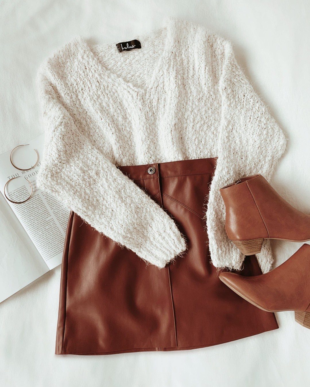 White fuzzy sweater and brown leather skirt paired with tan ankle booties and hoop earrings.