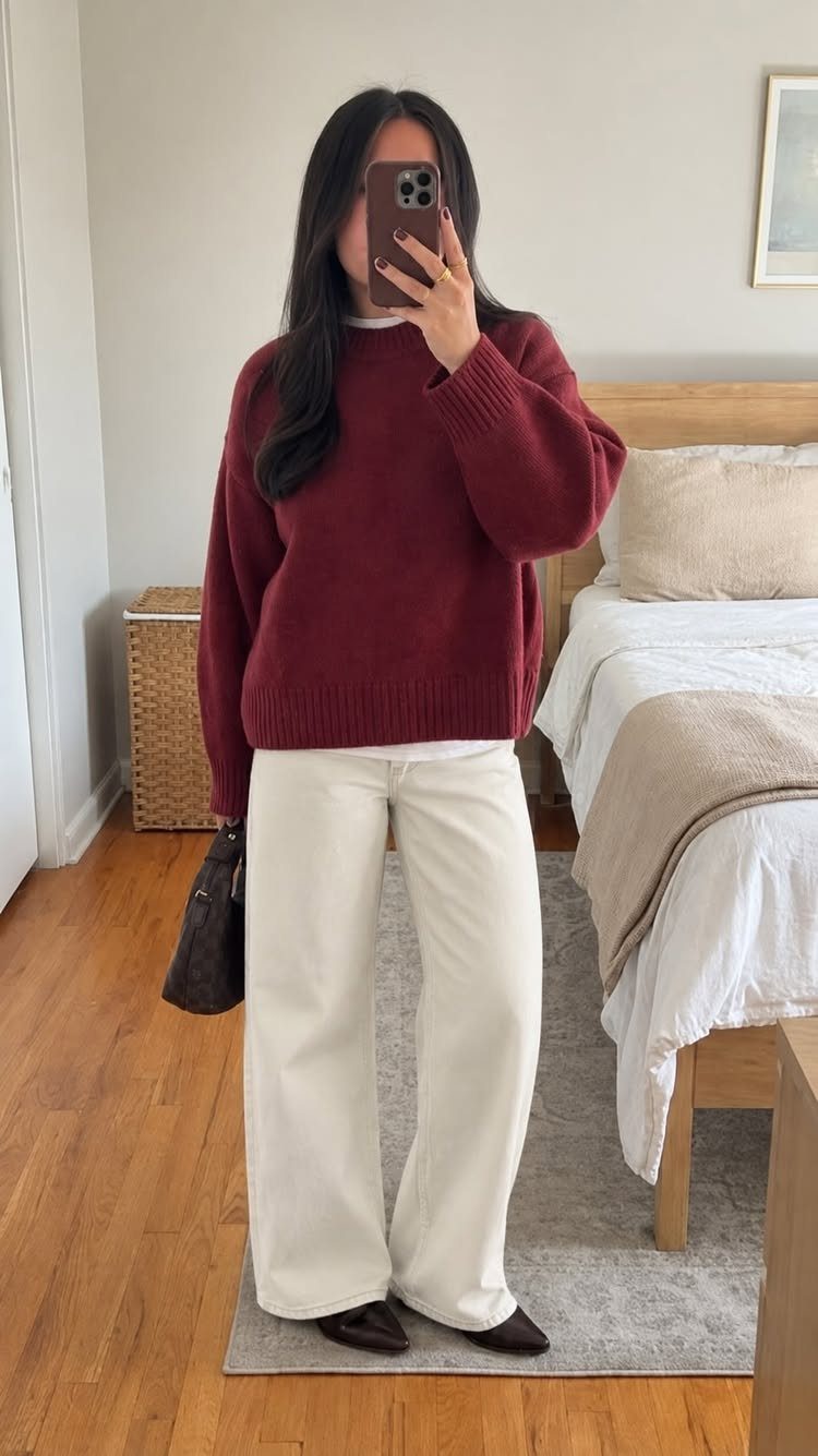 Woman in a burgundy sweater and cream wide-leg pants taking a mirror selfie.