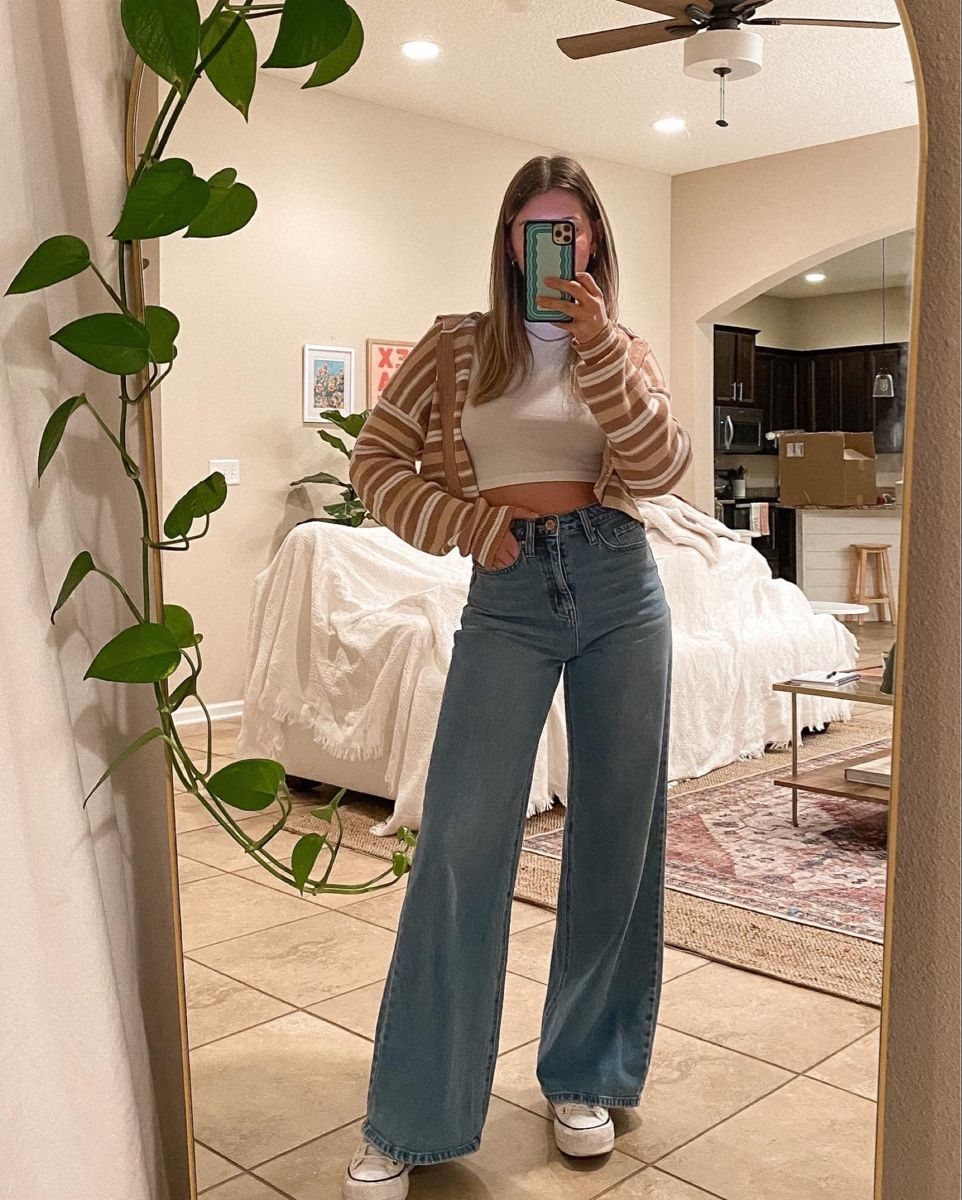 Woman in a white cropped top and wide leg jeans wearing white sneakers.