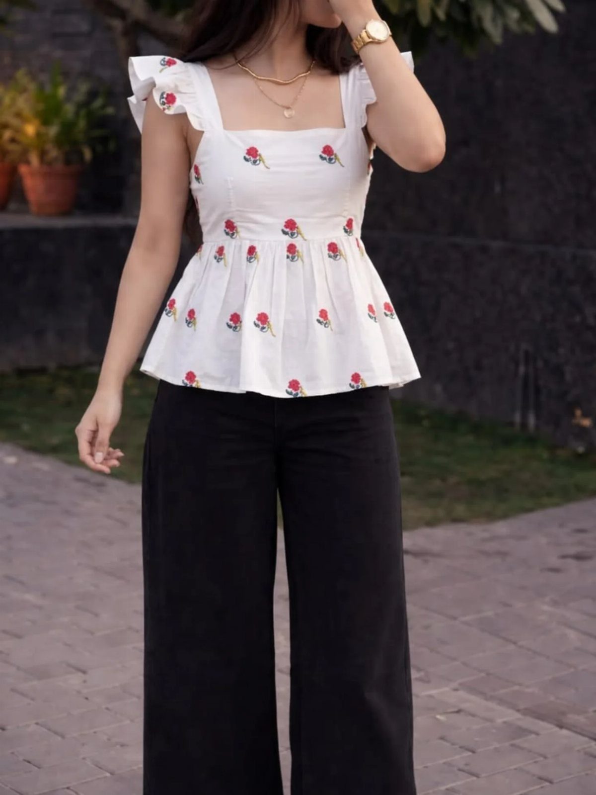 A person wearing a white floral peplum top and black wide-leg trousers standing outdoors.