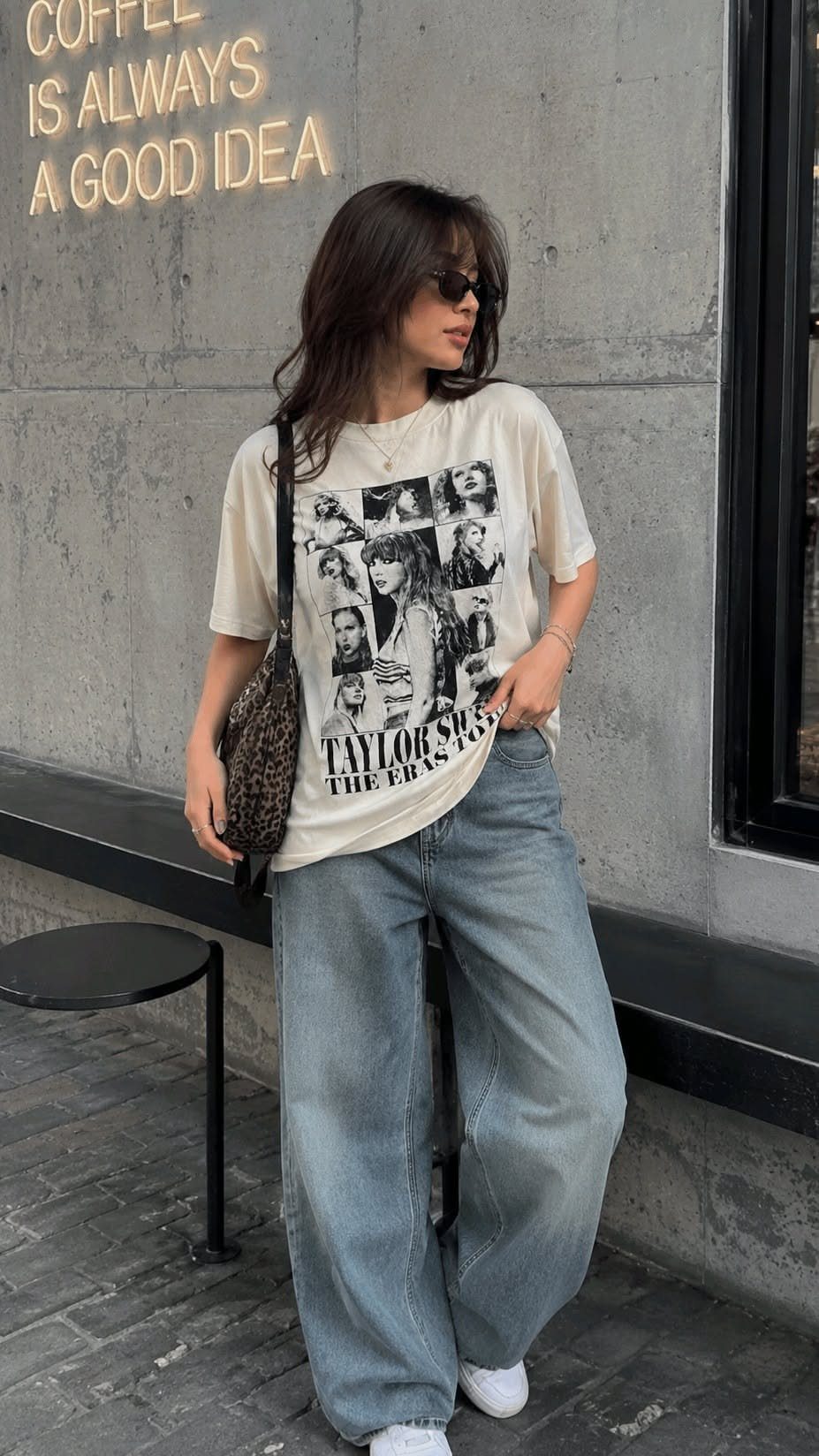 Woman wearing a cream graphic t-shirt and light blue wide-leg jeans standing outdoors.