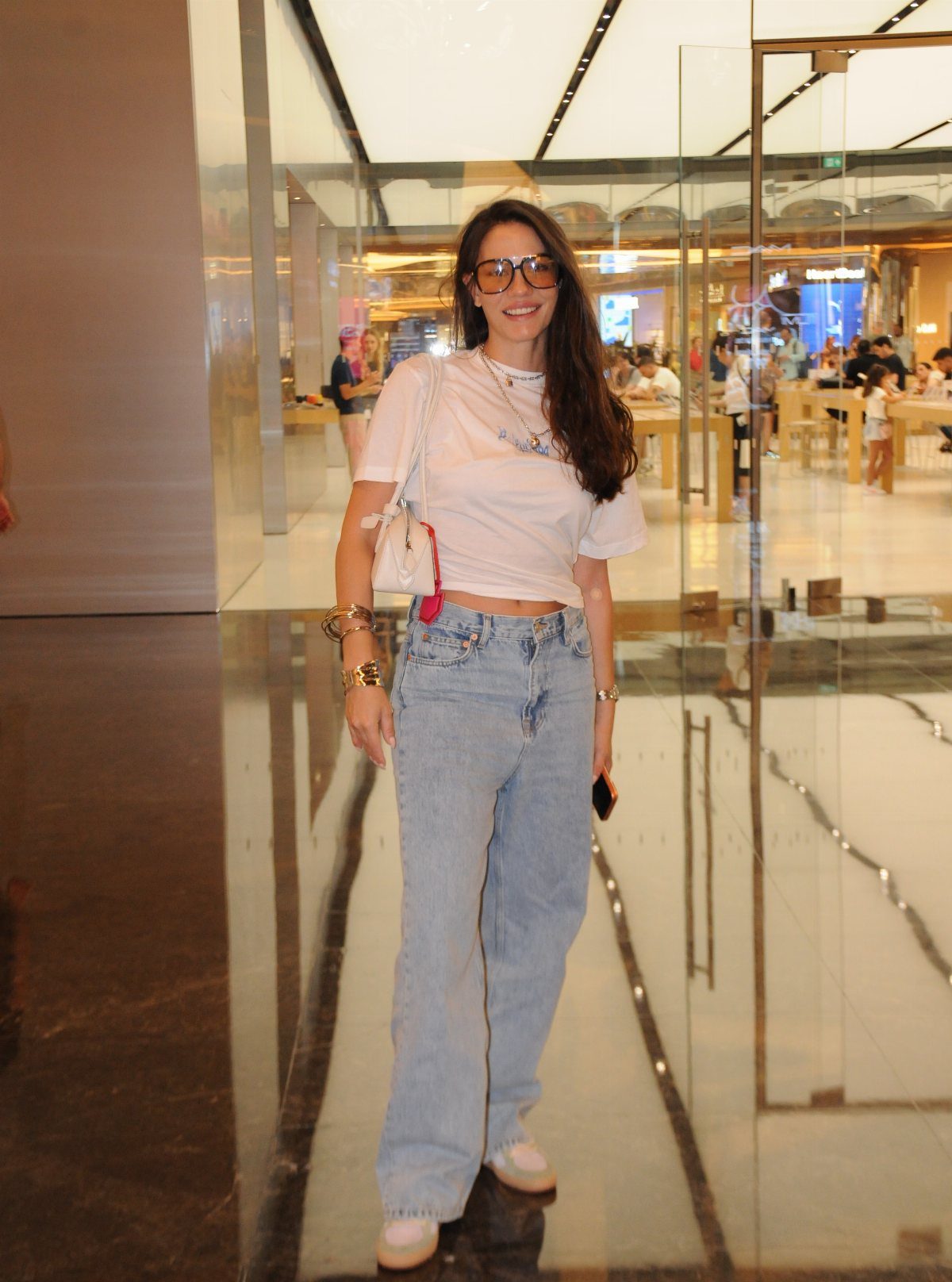 A woman wearing a white t-shirt and light blue wide leg jeans in a mall.