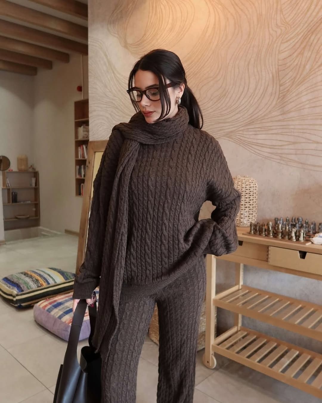 Woman wearing a brown cable-knit matching sweater and trousers set with a long scarf.