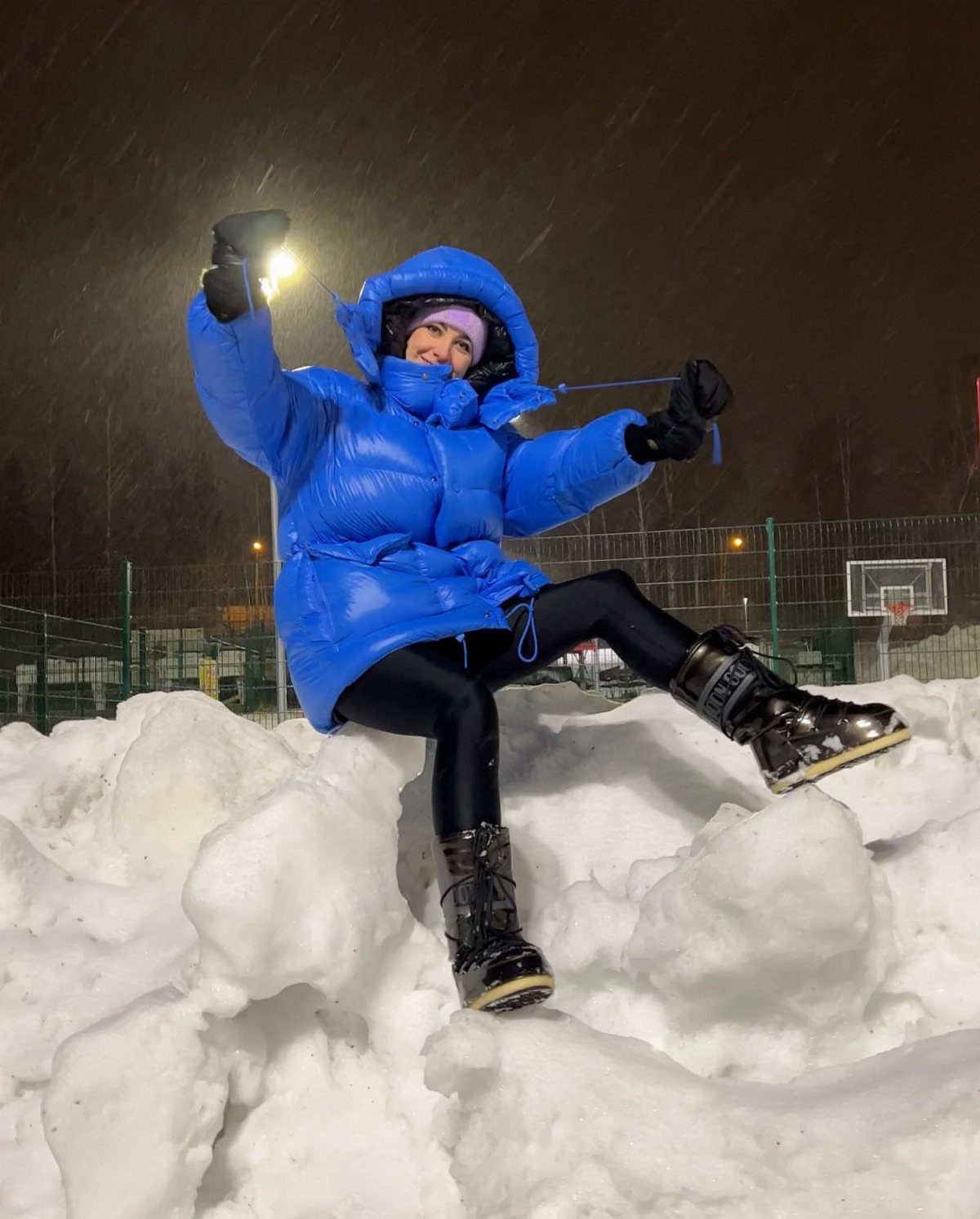 A person in a bright blue puffer jacket sitting on snow at night.