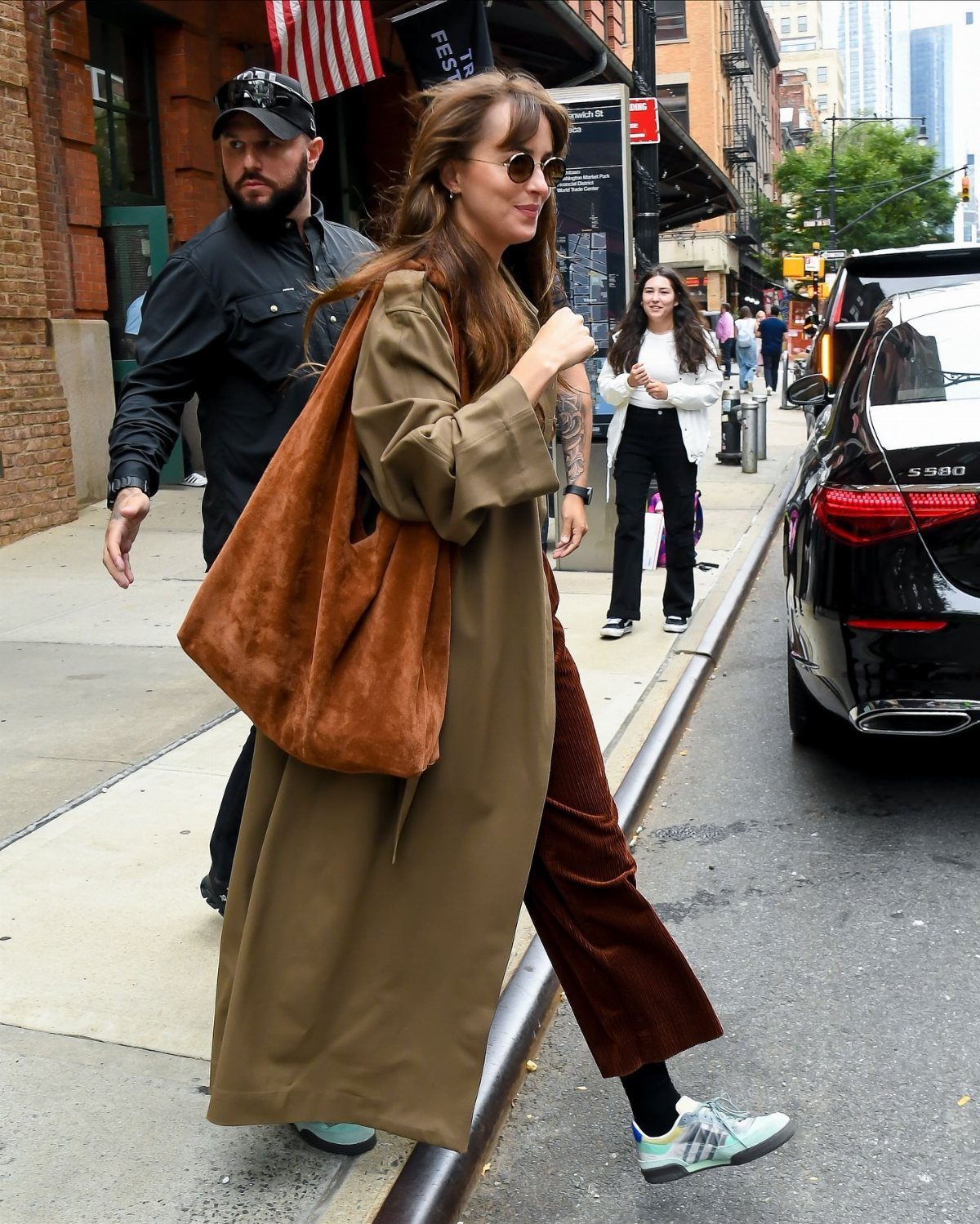 A woman walking down a city street carrying a large brown slouchy suede bag.