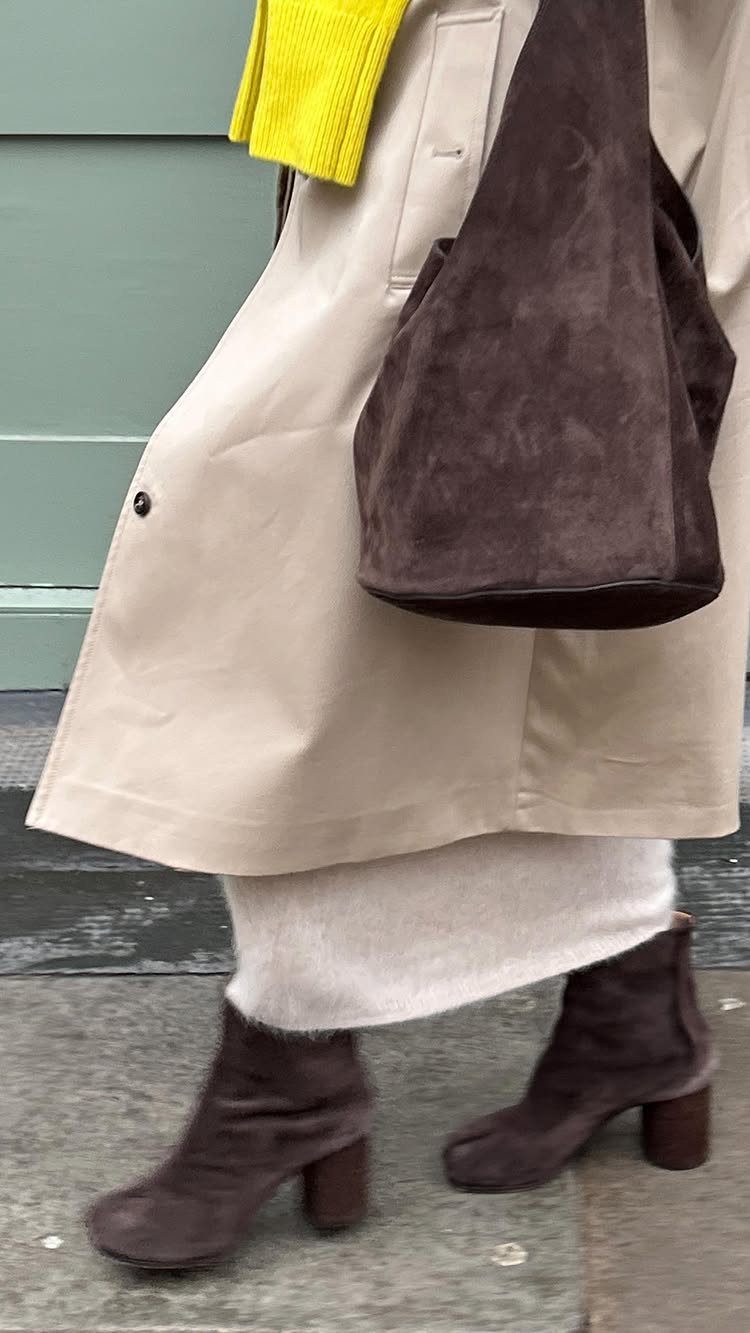 Person wearing a beige trench coat, white skirt, and dark brown suede heeled ankle boots.