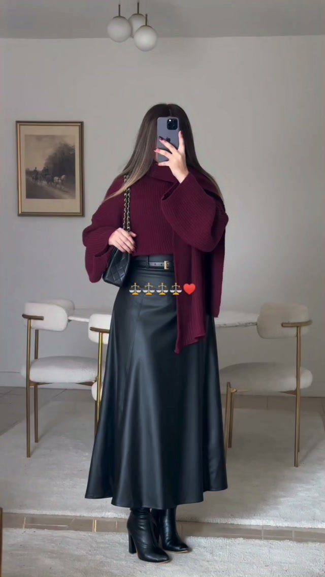 A person wearing a burgundy sweater and a black faux leather maxi skirt with black boots.