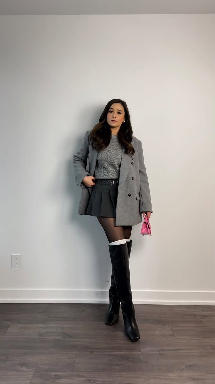 Woman wearing a grey coat, knit sweater, black skirt, tights, and tall black boots.