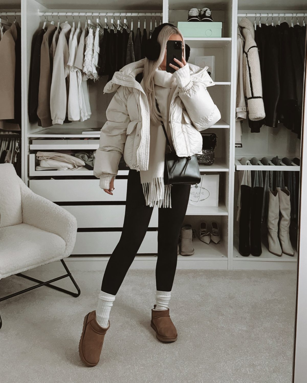 A person wearing a large white puffer coat, black leggings, and brown boots in a closet.