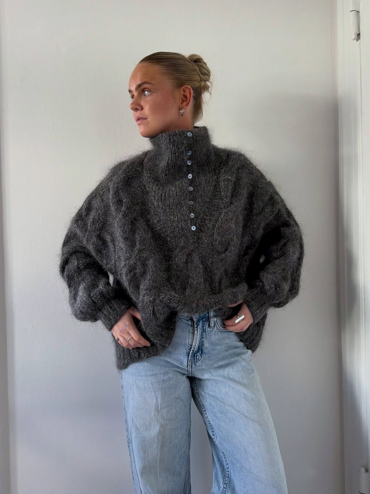 Woman wearing a dark grey chunky knit turtleneck sweater and light blue jeans.