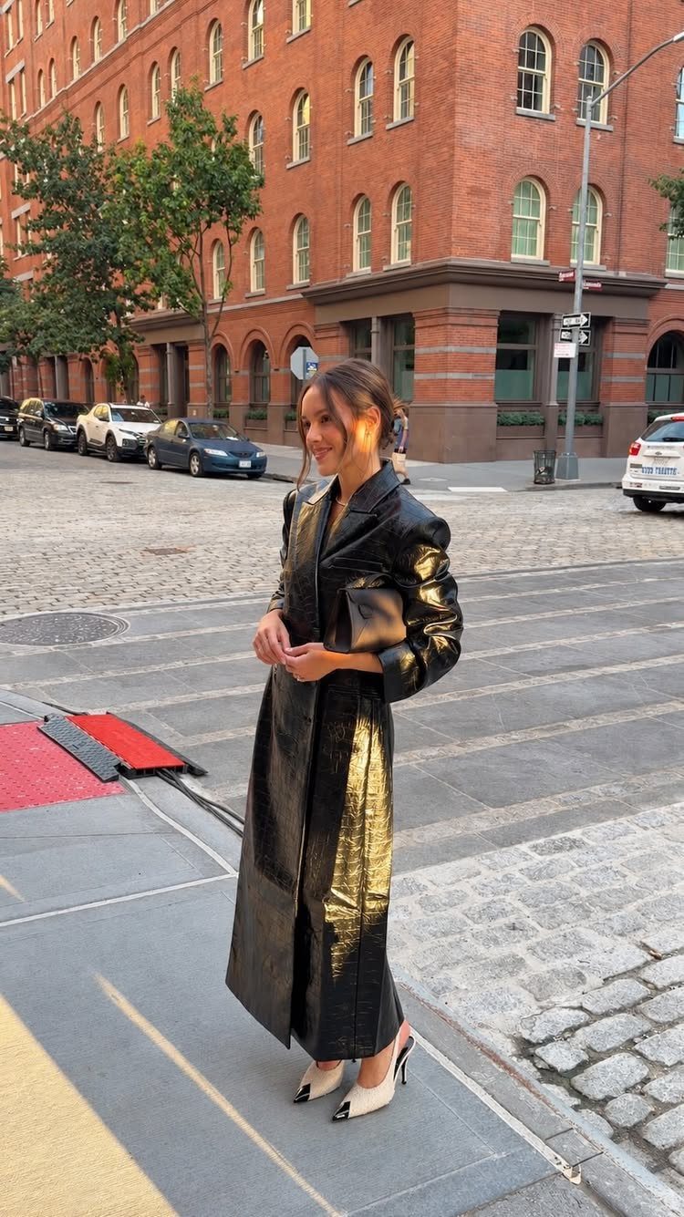 A woman in a long black textured coat and white heels standing on a city street.