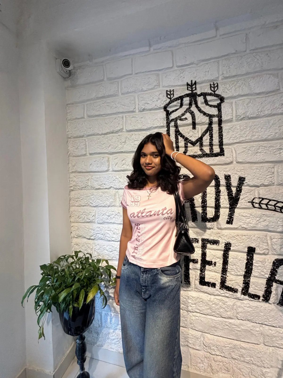 A woman wearing a pink graphic baby tee and baggy washed denim jeans posing indoors.