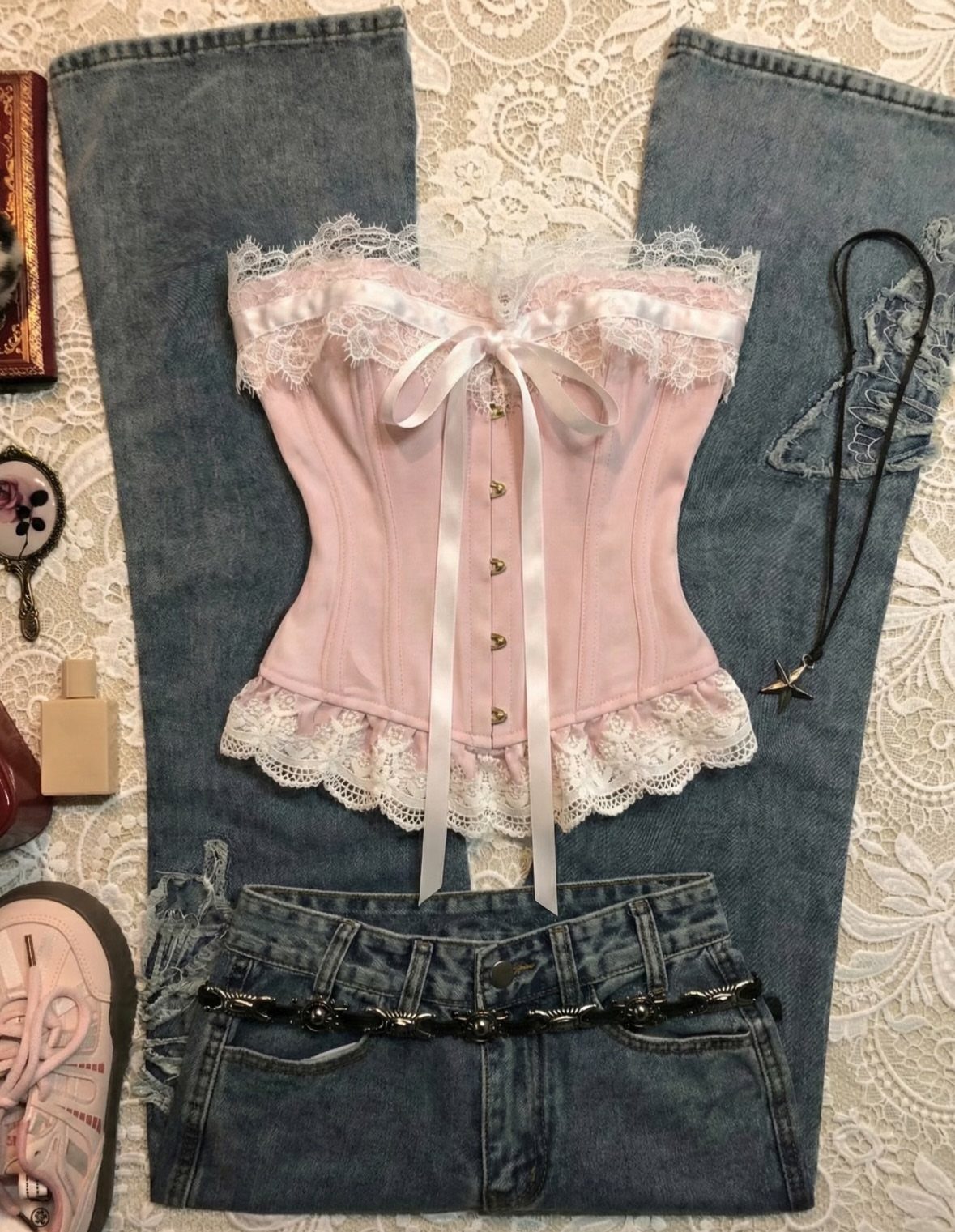 Pink lace corset and low-rise denim jeans laid on a white lace surface.